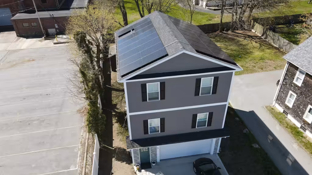 Aerial view of a modern two-story home with solar panels installed on the roof, surrounded by greenery and parking spaces, illustrating the benefits of solar energy for increasing home value in New England.