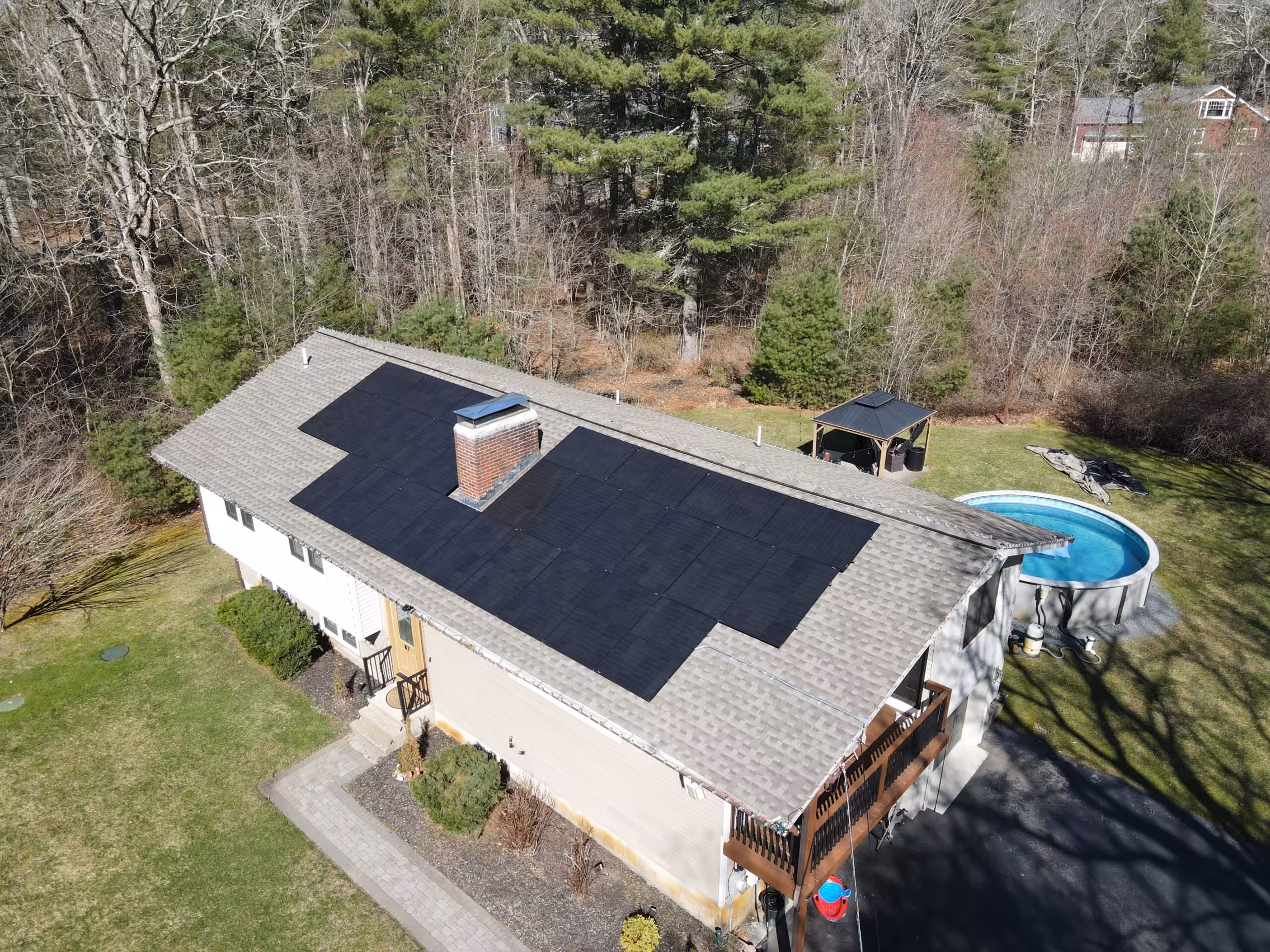 Aerial view of a house in Norton, MA, featuring a newly installed solar array on the roof, surrounded by a green yard and a pool, highlighting Sunfinity Power's solar installation services.