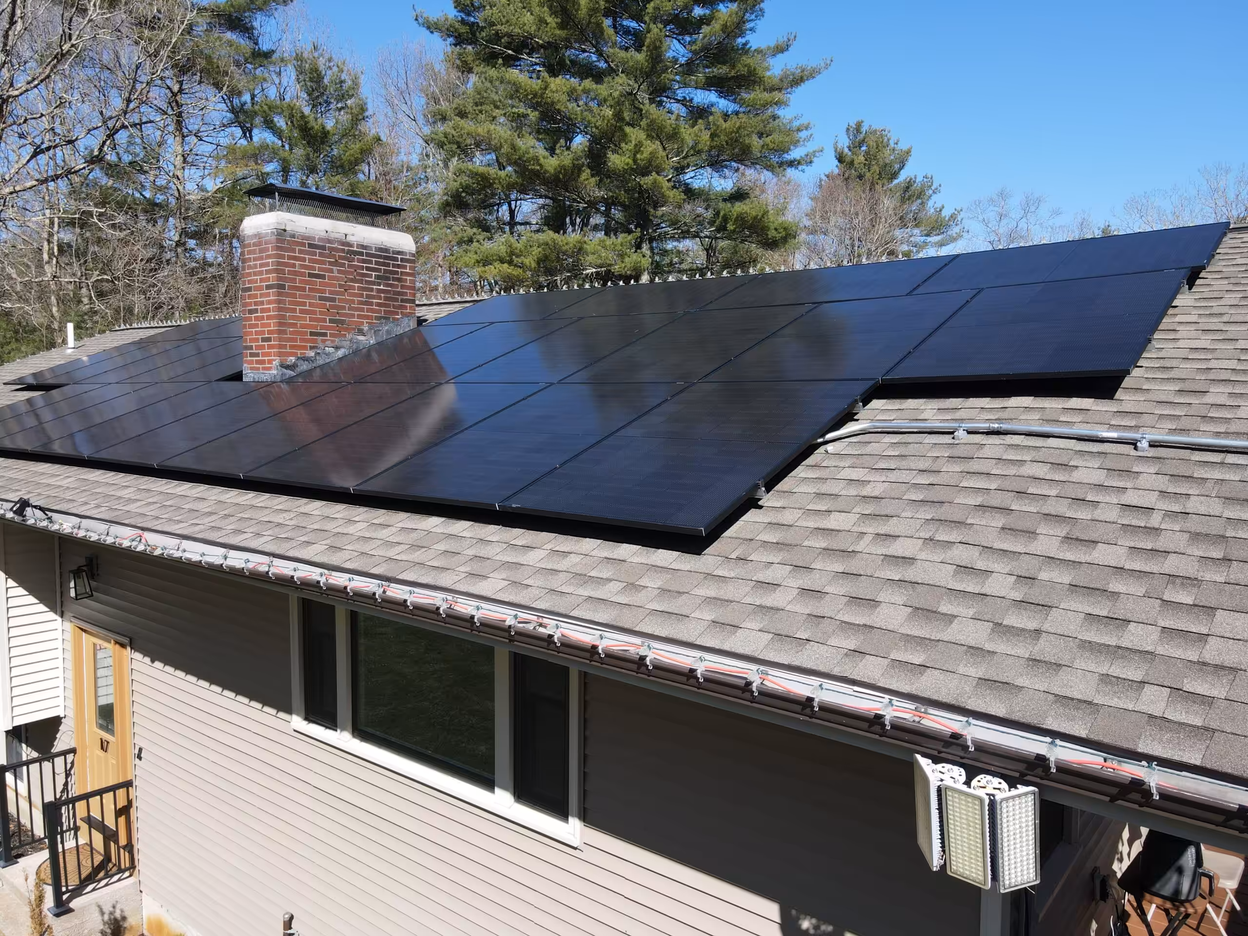 Rooftop solar panels installed on a house in Norton, MA, showcasing GAF Timberline shingles and a chimney, illustrating Sunfinity Power's bundled roofing and solar installation services.